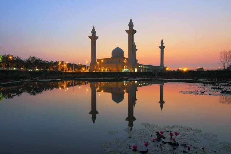 Beautiful mosque reflecting on lake at sunset, showcasing Islamic architecture.